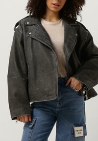 Grå læder jakke med kort længde, sølv hardware, lynlås lukning og brede manchetter. Sammen med blå denim cargo bukser med lappelommer.