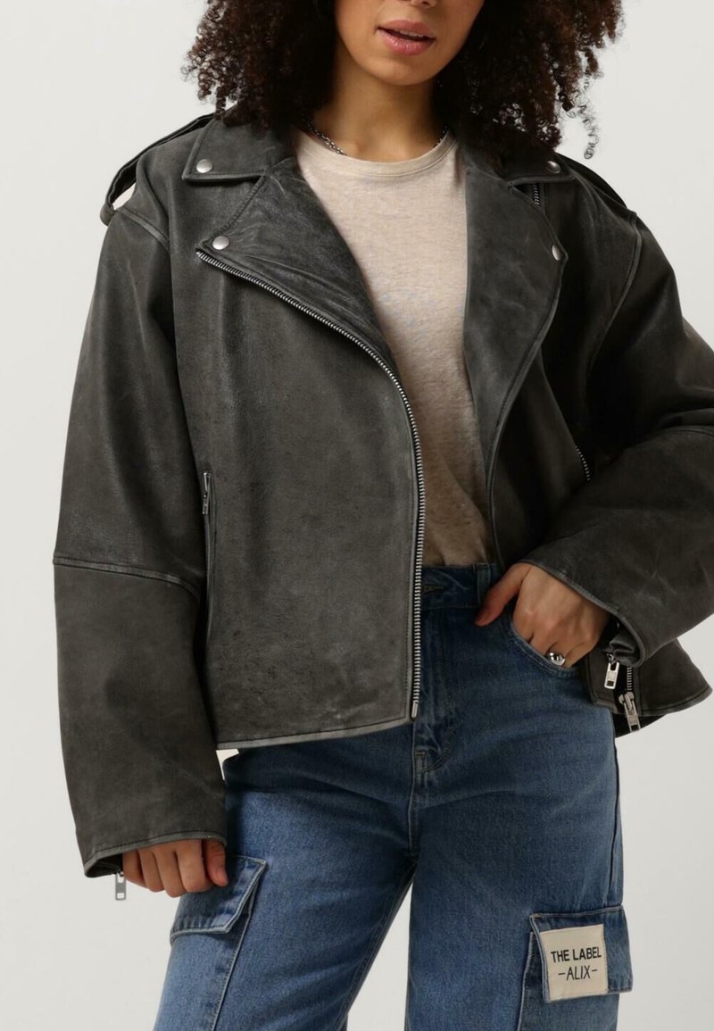 Grå læder jakke med kort længde, sølv hardware, lynlås lukning og brede manchetter. Sammen med blå denim cargo bukser med lappelommer.