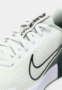 Tenisky Nike Air Max majú textúrovaný biely vrch, čierne logo a zelené akcenty s pohodlnou podrážkou. Šnúrky sú svetlo šedé.