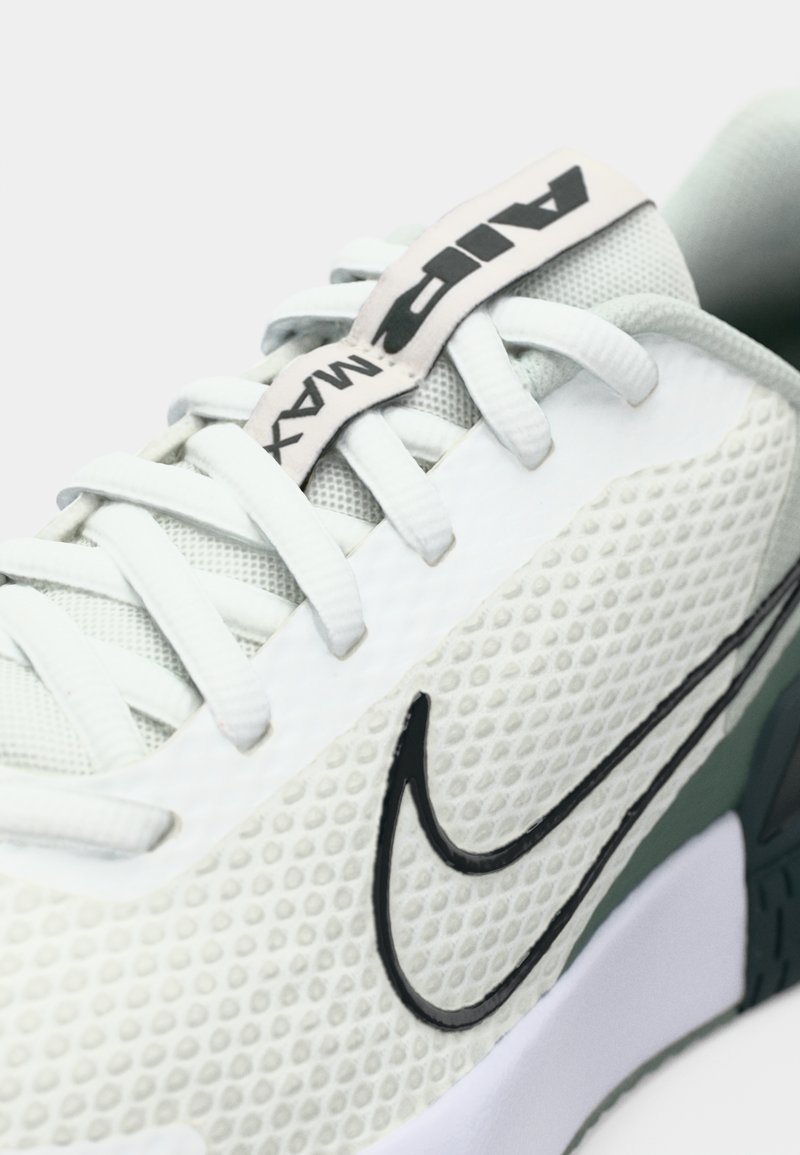 Las zapatillas Nike Air Max presentan una parte superior texturizada blanca, un logo negro y acentos verdes con una suela acolchada. Los cordones son de color gris claro.