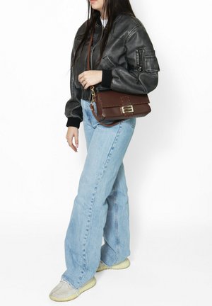 Braune Leder-Crossbody-Tasche mit rechteckiger Form, Schnallen-Detail und strukturierten Oberfläche. Kombiniert mit einer schwarzen Bomberjacke und hellblauen Jeans.