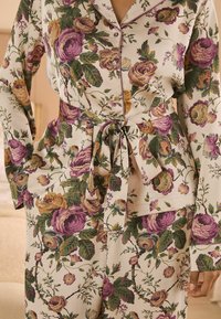 Set di pigiama floreale in crema con rose viola e gialle. Presenta una parte superiore con bottoni, vita con laccio e maniche lunghe, e pantaloni coordinati.