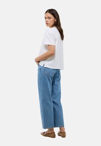 T-shirt en coton blanc à manches courtes, associé à un jean en denim bleu taille haute et ample. Les accessoires comprennent des chaussures plates marron.