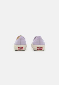 Baskets à enfiler en toile violette avec semelles en caoutchouc blanches et logo rouge au niveau du talon. Présentent des coutures minimales et un design à bout rond.