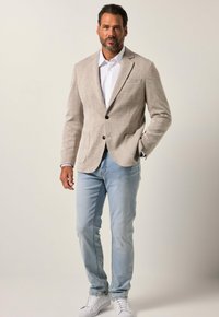 Beige ruudullinen bleiseri, jossa on viilennyskäänteet, yhden napin kiinnitys ja kaksi etutaskua, yhdistetty vaaleansinisiin farkkuihin ja valkoisiin tennareihin.