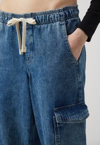 Joggers de mezclilla en azul claro con una cinturilla elástica y cordón. Presentan bolsillos laterales y un bolsillo tipo cargo en la pierna.