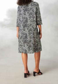 Abito paisley in bianco e nero con maniche a tre quarti, taglio al ginocchio e vestibilità comoda. Tacchi neri completano l'outfit.