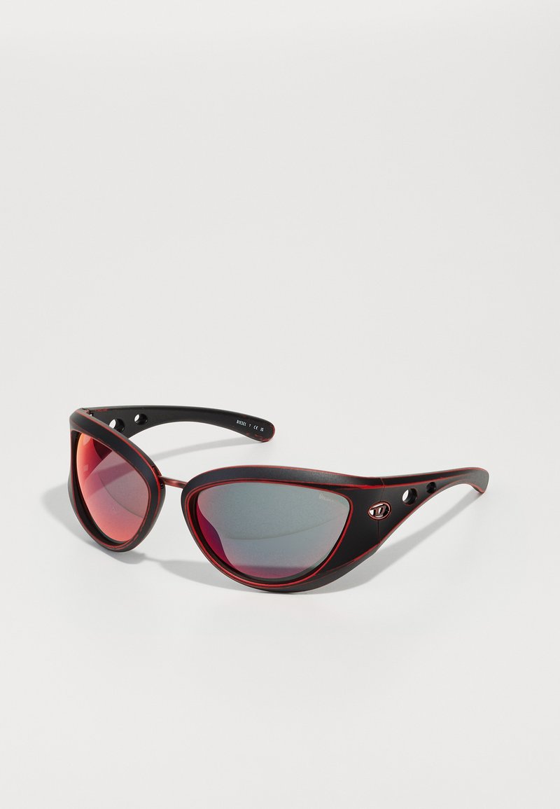 Óculos de sol pretos e vermelhos com uma forma audaciosa em cat-eye. Armações texturizadas mate e lentes refletoras com leve tonalidade. Inclui recortes nas hastes.