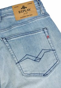 Ljusblå denimjeans bakficka med detaljer i mörkblå sömnad och en tanfärgad läderetikett med texten "REPLAY" vid midjan.