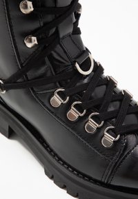Bottines en cuir noir avec œillets en argent, lacets noirs et semelle texturée robuste pour une meilleure adhérence et durabilité.