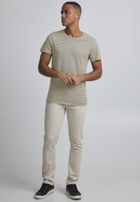 Lys beige stripete t-skjorte med rund hals, matchet med lyse jeans og svarte sneakers. Enkelt design, minimal detaljering.