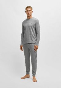 Grijze gebreide lange mouwen shirt met een ronde hals en logo op de borst, gecombineerd met bijpassende grijze broek. Gladde textuur, ontspannen pasvorm, geen patronen.
