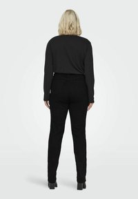 Mustat pitkähihaiset paidat ja korkeavyötäröiset mustat housut kapealla leikalla, valmistettu sileästä kankaasta, jossa on minimaalinen yksityiskohtaisuus.