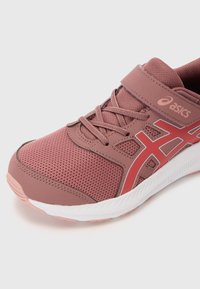 Chaussure de sport rose avec matériau en maille, fermeture à lacets et Velcro, semelle blanche et détails rouges. Empeigne texturée pour la respirabilité.