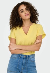 Geel V-hals top met korte mouwen, gemaakt van een gestructureerde stof. Gecombineerd met high-waisted blauwe spijkerbroek. Eenvoudig design, zonder patronen.