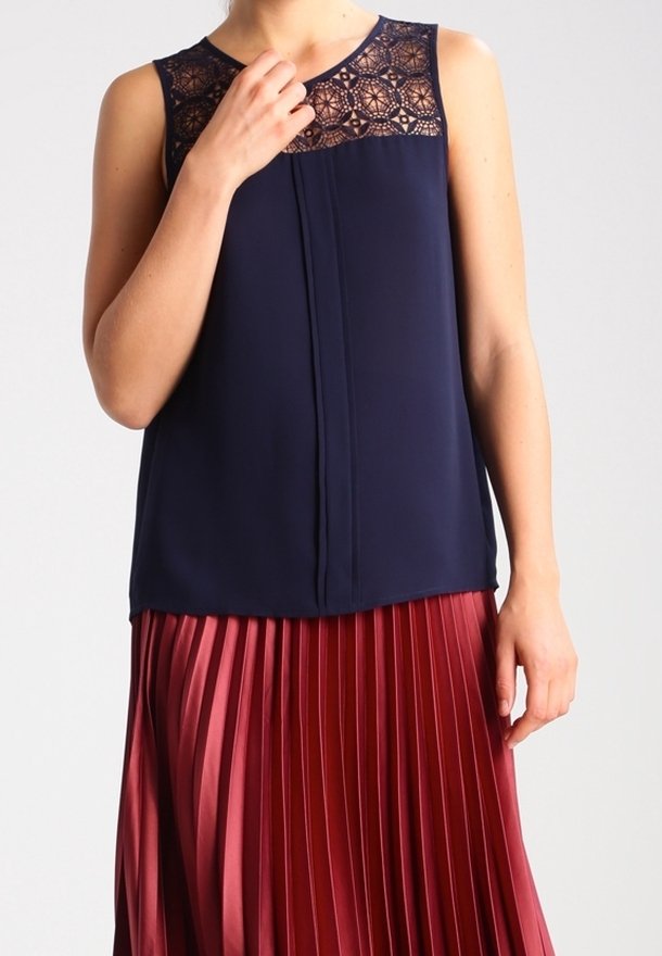 Haut sans manches bleu marine avec un empiècement en dentelle aux épaules, associé à une jupe bordeaux plissée. Tissu lisse avec des textures et des couleurs contrastées.