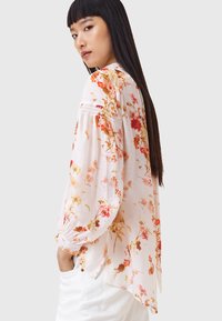 Bloemige blouse met lange mouwen in lichtroze, voorzien van meerkleurige bloemen, geplooide schouders en een ontspannen pasvorm; gecombineerd met witte broeken.