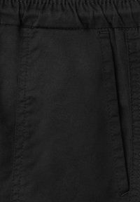 Gros plan d’un pantalon en tissu noir avec des coutures visibles et une ceinture élastique.