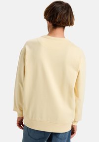 Light yellow sweatshirt with a relaxed fit, ribbed cuffs and hem, and a round neck. Soft texture, minimalistic design.