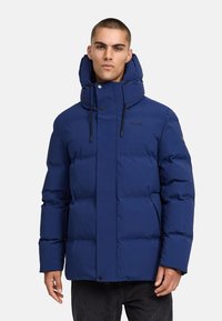 Modrá páperová bunda s vysokým golierom a nastaviteľnou kapucňou, s prešívaným vzorom, predným zapínaním na gombíky a dvoma bočnými vreckami.