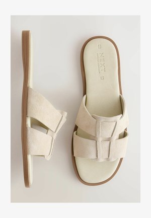 Beige Wildleder-Sandalen mit zwei breiten Riemen, weichem Fußbett und brauner Gummisohle. Mit geprägt eingestanztem Markenlogo auf dem Fußbett und minimalistischem Design.