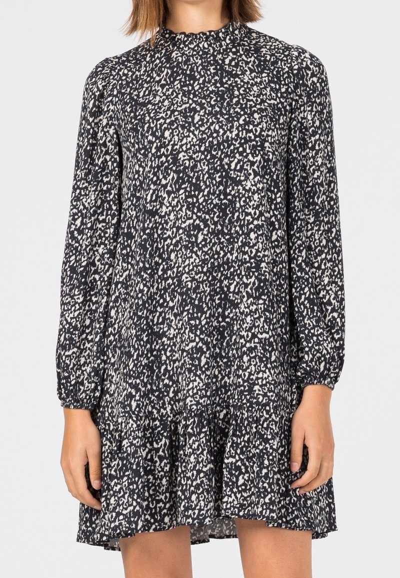 Femme portant une robe noire et blanche, à manches longues, longueur genou, à motif tacheté abstrait et ourlet volanté.