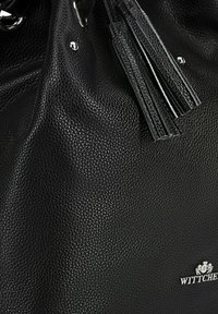Schwarze Lederhandtasche mit strukturierter Oberfläche, ausgestattet mit silberfarbenen Beschlägen und dekorativen Quasten. Prallendes Logo prominent dargestellt.