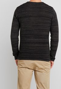 Maglione nero a trama con righe orizzontali, scollo rotondo e maniche lunghe, abbinato a pantaloni beige chiaro.