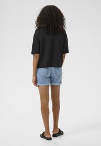 Black short-sleeved top, high crew neck, paired with light blue denim shorts. Model wears black slide sandals and has curly hair.
