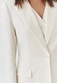 Lichtbeige linnen blazer met een gestructureerde afwerking, voorzien van een notch-kraag, twee knopen en een enkele borstzak.
