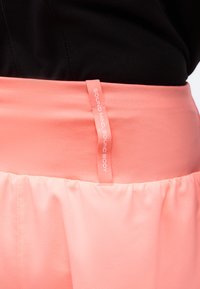 Κοντινό πλάνο της ροζ ζώνης μέσης σε φουστάνι ανοιχτό ροζ με κατακόρυφη υφασμάτινη ετικέτα που γράφει "SOUND MIND SOUND BODY" και μαύρο τοπ πάνω από τη ζώνη μέσης.