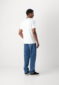 Camiseta blanca de algodón de manga corta combinada con unos vaqueros de mezclilla azul de corte holgado, con un clásico diseño de cinco bolsillos. Zapatillas negras completan el look.