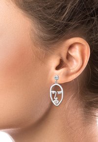 Orecchini a forma di volto in tonalità argento con design lineare minimalista, caratterizzati da un perno circolare e un contorno facciale astratto.