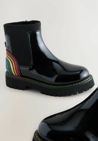 Botas de tobillo de charol negro con paneles laterales elásticos acanalados y un acento de rayas de colores en la parte trasera. Suela gruesa de goma texturizada.