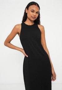 Rochie neagră fără mâneci, confecționată dintr-un material neted, cu un design ajustat și un ușor sclipici. Prezintă un decolteu rotund și buzunare laterale.