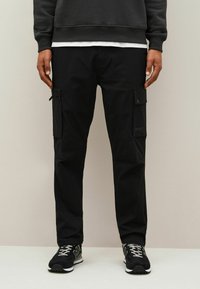 Svarta cargobyxor tillverkade av slitstark tyg, med flera sidofickor och en avslappnad passform. Matchade med svarta sneakers och en mörk sweatshirt.