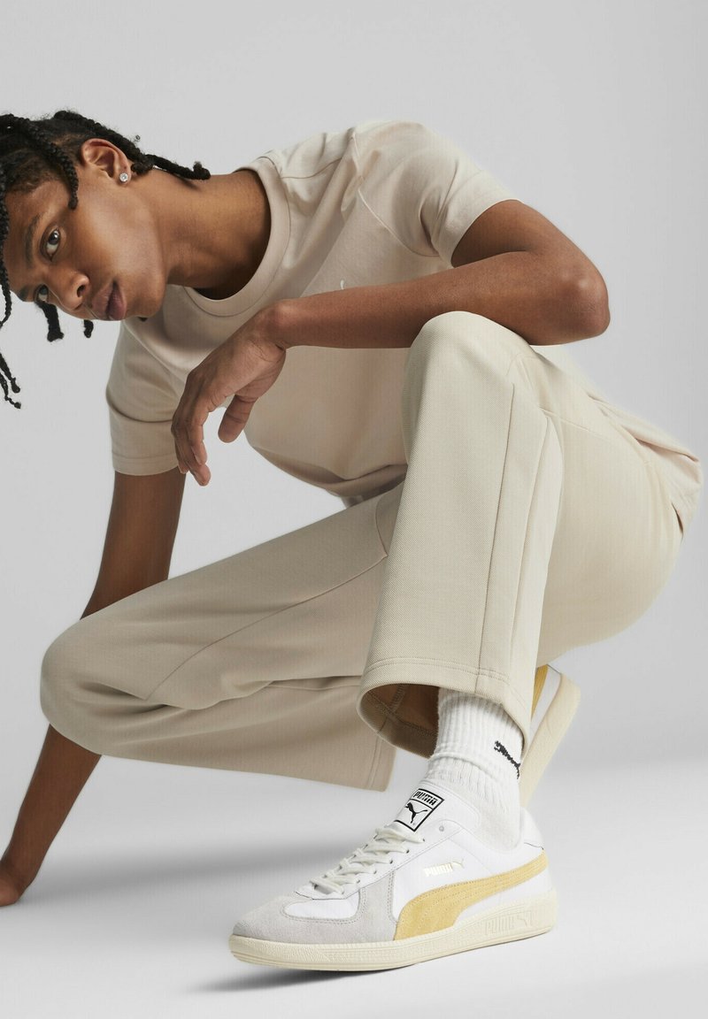 Beige t-shirt och byxor med slät textur, kombinerat med vita och gula Puma-sneakers med strukturerad sula och logotypdetalj.