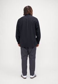 Maglietta nera a maniche lunghe, pantaloni cargo grigi, sneakers bianche e nere. Presenta una vestibilità comoda con un design semplice e un tessuto resistente.
