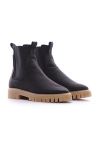 Botas Chelsea negras de lona con paneles laterales elásticos, puntera puntiaguda y suela de goma gruesa de color marrón claro con textura estriada.