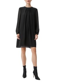 Czarna sukienka z długimi przezroczystymi rękawami, plisowanym dekoltem i luźnym krojem. Para czarnych botków na wysokim obcasie z ostro zakończonym noskiem.