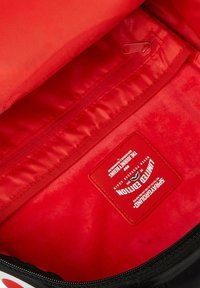 Interior de bolsa negra con un forro rojo brillante. Presenta un bolsillo con cremallera y una etiqueta que dice "Edición Limitada". Textura suave y lisa.