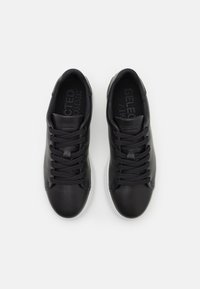 Mustat nahkasneakerit, joissa on pyöreä kärki, pehmustettu kieli ja litteät nauhat. Valkoinen kumipohja ja kohokuvioitu brändilogo kantapäässä.