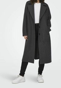 Grijze wolblend lange jas met een notch-kraag, dubbele knoopsluiting, zijzakken en een relaxte pasvorm, gecombineerd met zwarte jeans en witte sneakers.