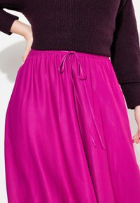 Fuksia midi-hame, jossa on sileä pinta, elastinen vyötärö ja nyöritys, yhdistetty tumman violetin neulepaidan kanssa.