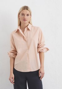 Helles rosa Button-Down-Hemd aus weicher Baumwolle, mit langen Ärmeln, die an den Bündchen aufgerollt sind, einem klassischen Kragen und abgerundetem Saum.