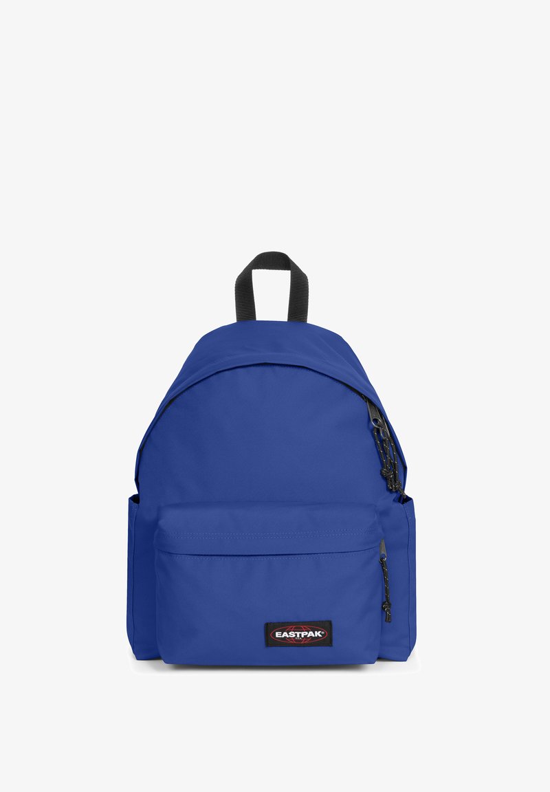 Mochila de tela azul con forma redondeada, bolsillo frontal con cremallera, correas de hombro ajustables y un asa en la parte superior. Presenta un parche del logo de Eastpak.