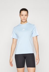 Camiseta atlética de color azul claro con mangas cortas, que presenta detalles de tres rayas blancas y un pequeño logo blanco en el pecho. Pantalones cortos ajustados negros.