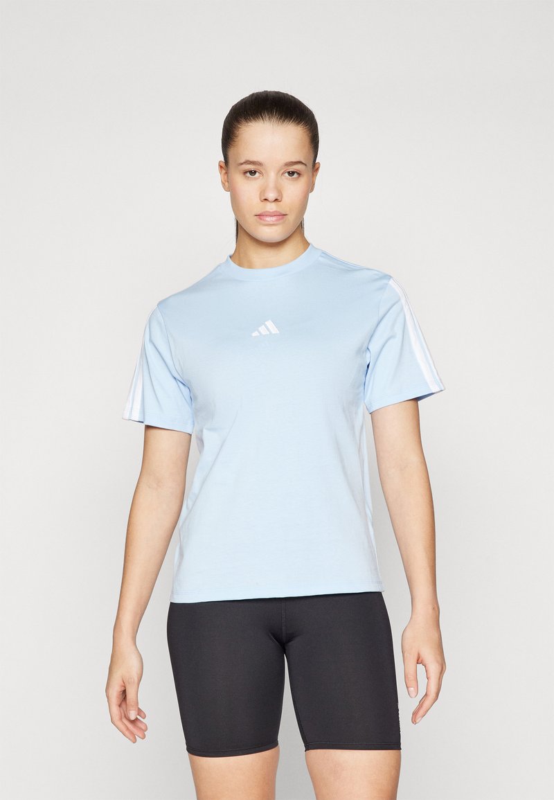 Camiseta atlética de color azul claro con mangas cortas, que presenta detalles de tres rayas blancas y un pequeño logo blanco en el pecho. Pantalones cortos ajustados negros.