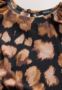 Blouse à encolure ronde avec imprimé animal abstrait noir, marron et beige et petite fermeture à bouton noir dans le dos.
