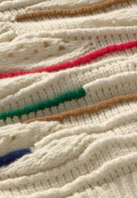 Stricktextil in Creme mit welliger Textur. Verfügt über fünf horizontale Streifen in Rot, Grün, Braun und Blau. Weiches, wollartiges Material.